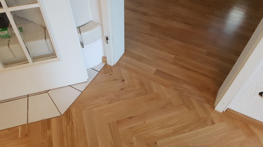 Eiche massiv Parkett, 22mm stark, im Fischgrat Verband verlegt und endbehandelt. Inkl. Fußleistenmontage.
