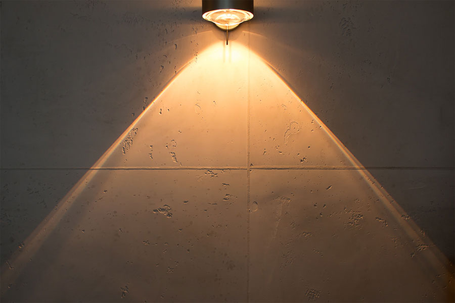 Detailaufnahme eines warmen Lichtkegels auf handgefertigtem Kalkputz in Beton-Optik.